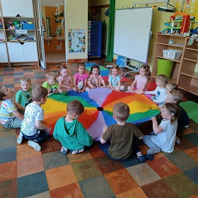 Dzieci siedzą na podłodze wokół kolorowej chusty animacyjnej