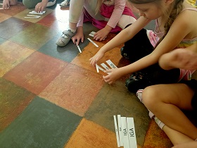 Dziewczynki układają z karteczek z imionami wieżę, od najmniejszej karteczki do największej.