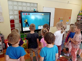 Dzieci stoją przed monitorem, na którym wyświetlany jest film. 