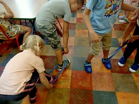 Czworo dzieci ma założone szarfy na nogi i wspólnie w parach idą po sali. 