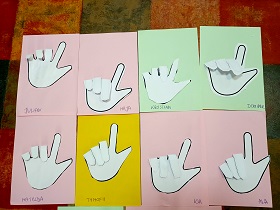 Osiem prac plastycznych leży na podłodze. Są to papierowe dłonie ułożone w znak love w języku migowym.