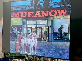 Na ekranie telewizora widać dzieci, które znajdują się pod kinem Muranów.