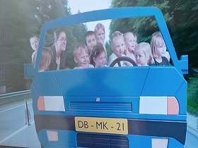 Na ekranie telewizora widać dzieci i panią, które znajdują się w samochodzie i nim kierują.