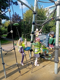 Piątka dzieci w odblaskowych kamizelkach bawi się na sprzętach na placu zabaw. 