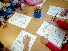 Piątka dzieci siedzi przy stoliku i koloruje kolorowanki.