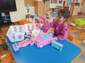 Dwie dziewczynki bawią się lalkami, autem i innymi akcesoriami przy stoliku