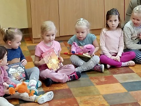 6 dziewczynek siedzi na podłodze. Jedna z dziewczynek prezentuje przyniesioną książkę o "Lwiej straży". Pozostali jej się przyglądają. 