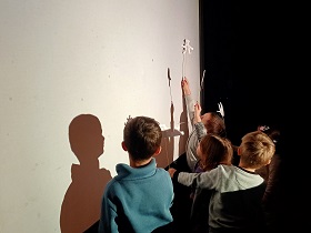 Dzieci stoją za białym ekranem i pokazują szablony przyczepione do patyczków.