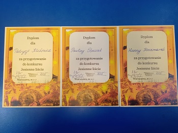 Na niebieskim tle leżą trzy dyplomy za przygotowanie dzieci do udziału w konkursie „Jesienne liście”.