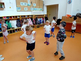 Dzieci w strojach sportowych ćwiczą w szatni obroty. 