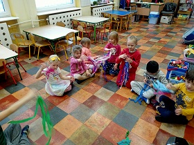 Na podłodze dzieci siedzą obok siebie i ruszają swoimi kubkami z doczepionymi bibułami. 