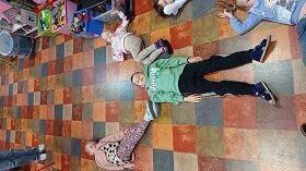 Dwie dziewczynki i chłopiec tworzą znak litery Y leżąc na podłodze.
