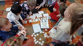 Dzieci szukają litery K wśród rozsypanych liter alfabetu. 