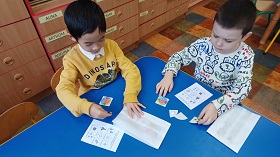 Chłopiec w żółtej bluzie i chłopiec w bluzie w pieski siedzą przy niebieskim stoliku i grają w zrobioną przez siebie grę sensoryczną. 