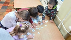 Dzieci stoją przy stoliku i szukają litery R wśród rozsypanych liter alfabetu.