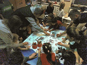 Na stoliku rozłożony jest papierowy obrus ze świątecznymi obrazkami. Dzieci wraz z rodzicami kolorują go.
