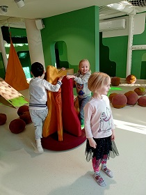 Troje dzieci bawi się w sali sensorycznej i kręci się na okrągłej zabawce.