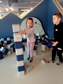 Dziewczynka i chłopiec budują wieżę z klocków magnetycznych. 