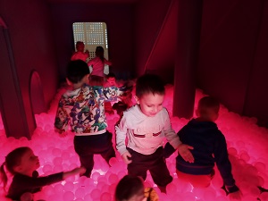 Dzieci bawią się w podświetlonej na czerwono sali z plastikowymi kulkami. 