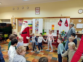 Dzieci z Paniami i Świętym Mikołajem tańczą w kole trzymając się za ręce.