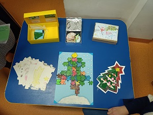 Na niebieskim stoliku leżą prace konkursowe wykonane przez dzieci. Są to puzzle o tematyce świątecznej.