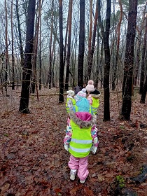 Dzieci w zimowych strojach oraz kamizelkach odblaskowych stoją w lesie.