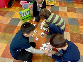 Czworo chłopców siedzi na podłodze i łączy ze sobą drewniane puzzle. 