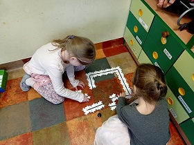 Dwie dziewczynki siedzą na podłodze i układają drewniane puzzle.