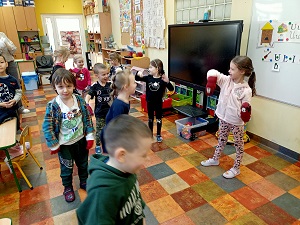 Dzieci tańczą na podłodze mając nałożone na dłonie rękawiczki. 