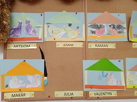Na tablicy korkowej wiszą prace dzieci. Prace przedstawiają kolorowe ptaki siedzące w karmniku. 