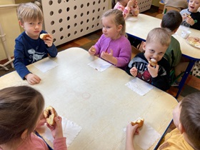 Piątka dzieci siedzi przy stoliku i je pączki