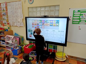 Chłopiec stoi przy monitorze i dopasowuje obrazki do odpowiednich kolumn. 