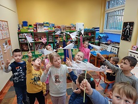 Dzieci pokazują wykonane przez nie latające bociany z papieru na słomce. 
