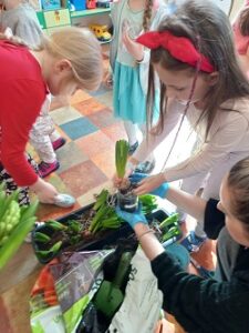 W dużych donicach ułożone są cebulki hiacyntów. Dzieci czekają ze słoiczkami, aby zasadzić swojego kwiatka. 