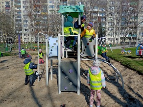 Dzieci wspinają się na zabawki na placu zabaw. Dzieci są ubrane w kamizelki odblaskowe. 