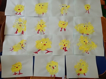Zdjęcie przedstawia 15 prac wykonanych przez dzieci. Na pracach widnieje żółty kurczaczek, z doklejonymi oczkami i namalowanymi czerwonymi nóżkami i dzióbkiem. 