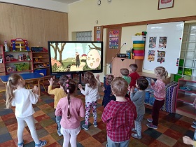 Dzieci stoją przed ekranem i tańczą- dekorują ruchem pisankę. Na ekranie widać Panią, która demonstruje ruchy i pisankę. 