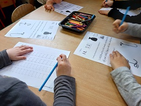 Dzieci siedzą przy stoliku i rozwiązują karty pracy z literą Ł. 