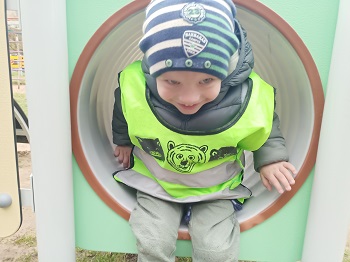 Uśmiechnięty chłopiec w ciemnozielonej kurtce i czapce w paski wychodzi z tunelu znajdującego się na jednej z konstrukcji. 
