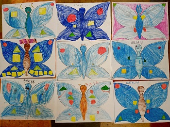 Na podłodze znajdują się prace plastyczne dzieci przedstawiające niebieskie motyle z figurami geometrycznymi. 
