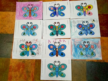 Na podłodze znajdują się prace plastyczne dzieci przedstawiające niebieskie motyle z figurami geometrycznymi. 
