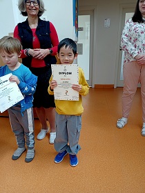 Chłopiec stoi obok dwóch pań i trzyma w dłoniach dyplom. Obok niego stoi chłopiec z dyplomem.
