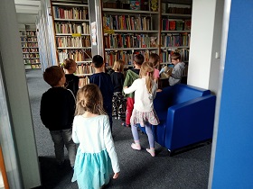 Dzieci chodzą po bibliotece wśród regałów.