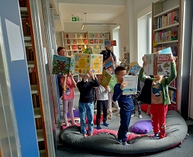 Dzieci stoją z otwartymi książkami uniesionymi w górze.