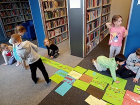 Dzieci układają kolorowe kartki z rysunkami na dywanie.