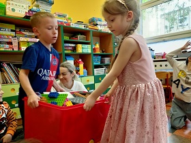 Chłopiec i dziewczynka przenoszą wspólnie kosz z klockami lego. 