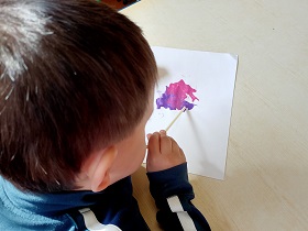 Chłopiec dmucha przez słomkę na plamę farby rozlanej na kartce. 