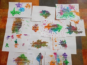 Prace plastyczne dzieci rozłożone na podłodze, przedstawiające wykonane z farby zarazki z oczami. 