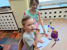 Dwie dziewczynki pracują nad tworzeniem własnej książki z wykorzystaniem fioletowych piórek.