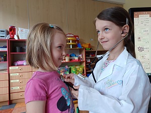 Dziewczynka przebrana za lekarza za pomocą stetoskopu słucha bicia serca dziewczynki w różowej koszulce. 